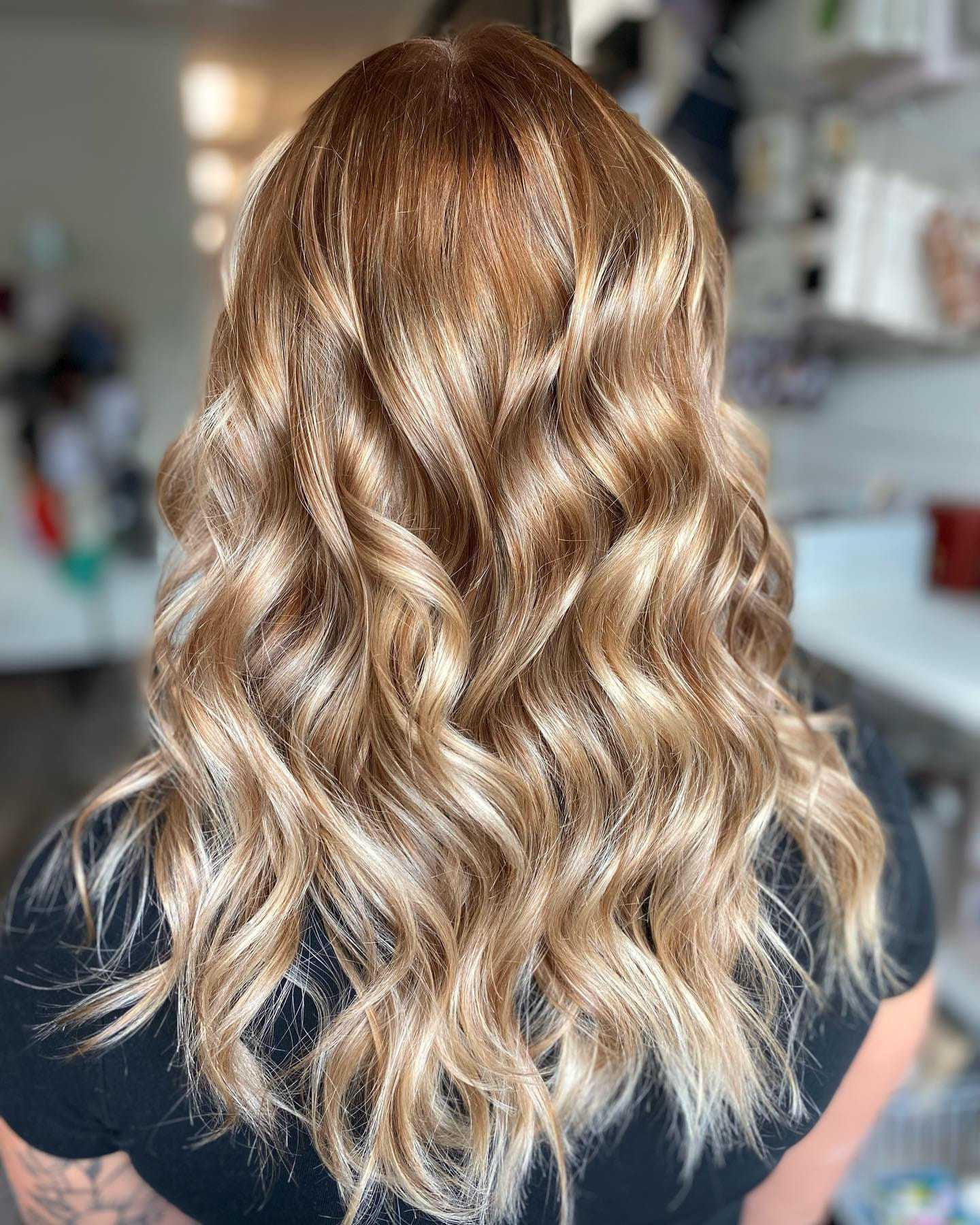 Back view of a person with wavy, shoulder-length, blonde hair in a well-lit room.