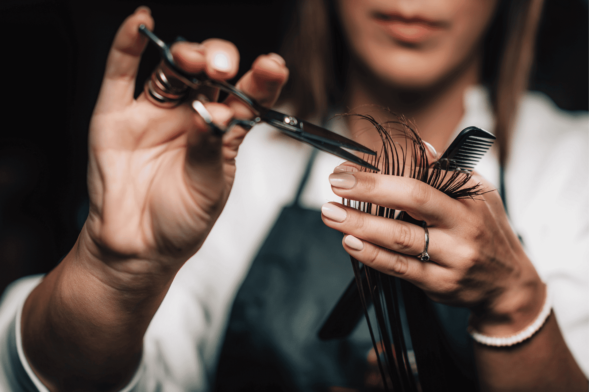 Close-up of a hairdresser cutting hair with scissors and comb.