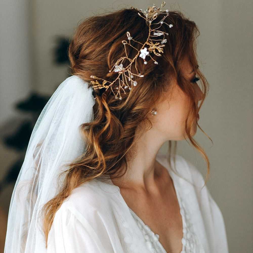 Bride with a floral headpiece and veil, looking to the side, in a white wedding dress.