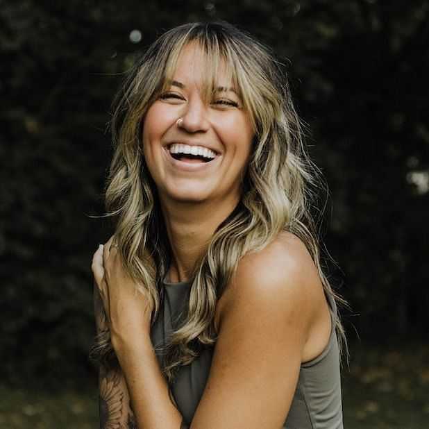 Woman laughing outdoors with long hair, wearing a sleeveless top.