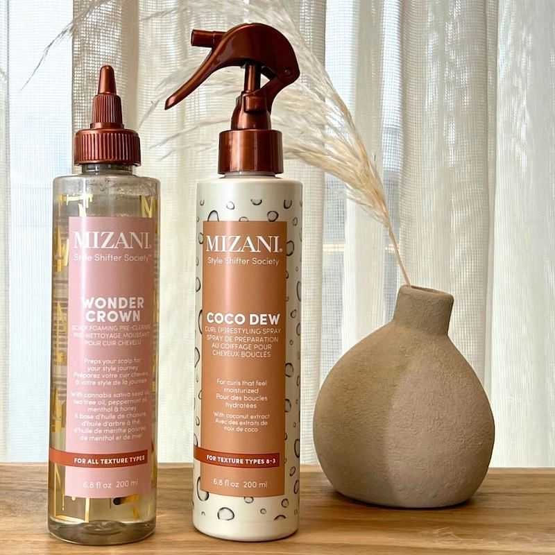 Two Mizani hair care products on a wooden table with a decorative vase and dried grass.