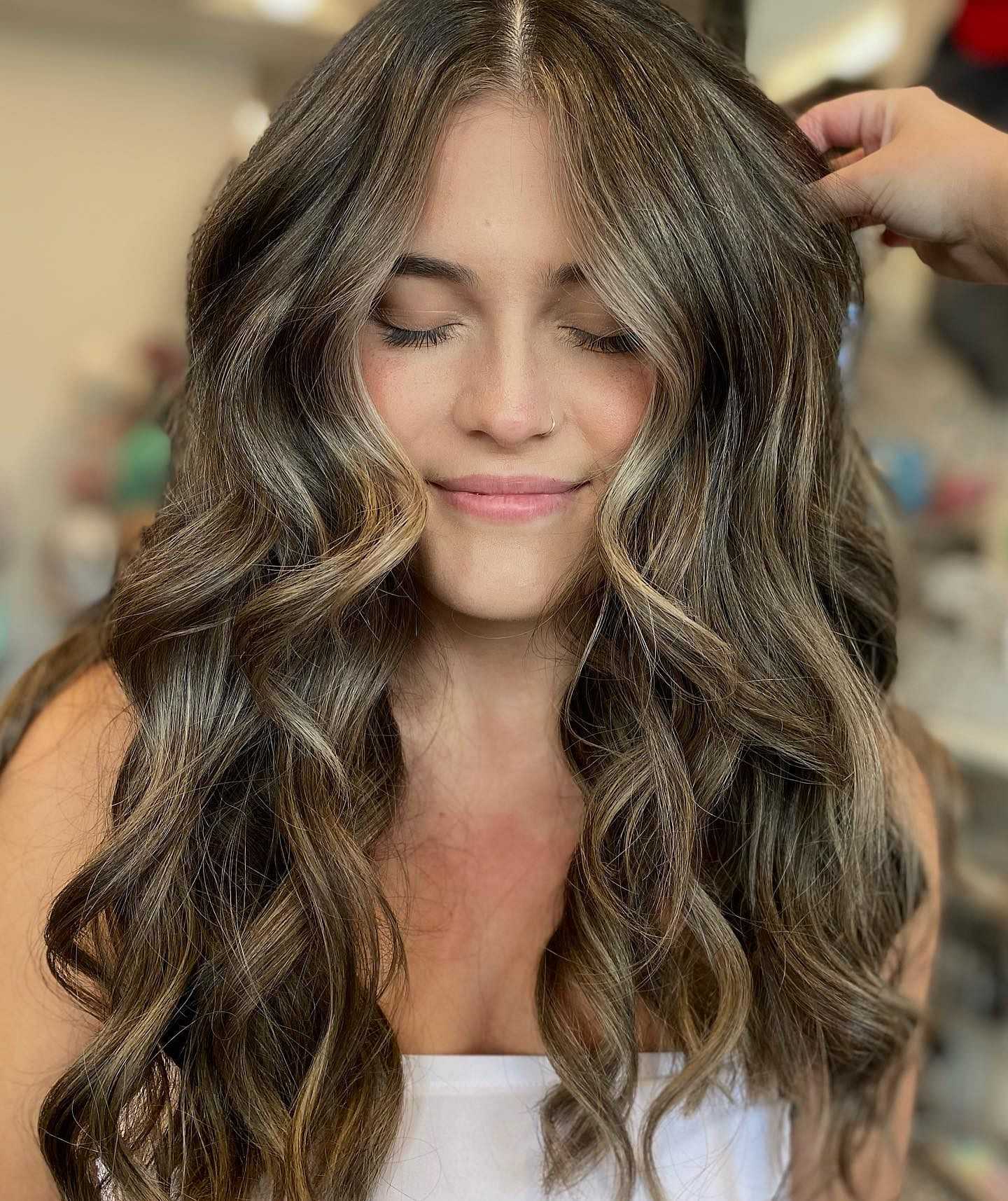 Woman with long, wavy hair getting a hairstyle touch-up in a salon.